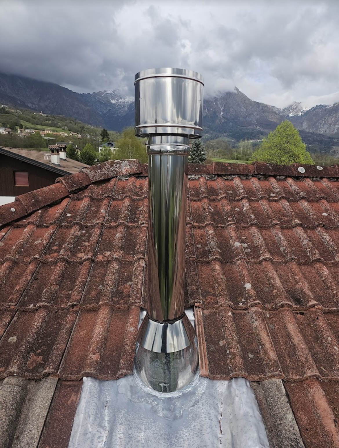 Canna fumaria inox lucido su tetto in coppi con vista montagne